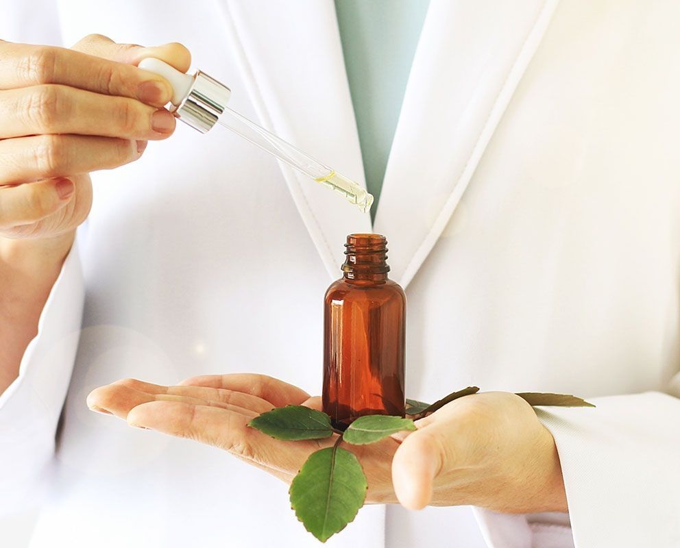 Person mit weißem Kittel hält eine Pipette über ein Gläschen